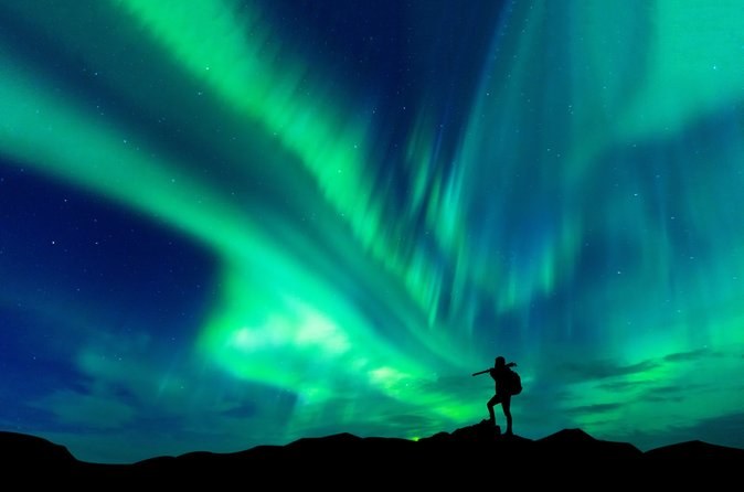 A silhouette on a ridge pointing up at bright aurora curtains