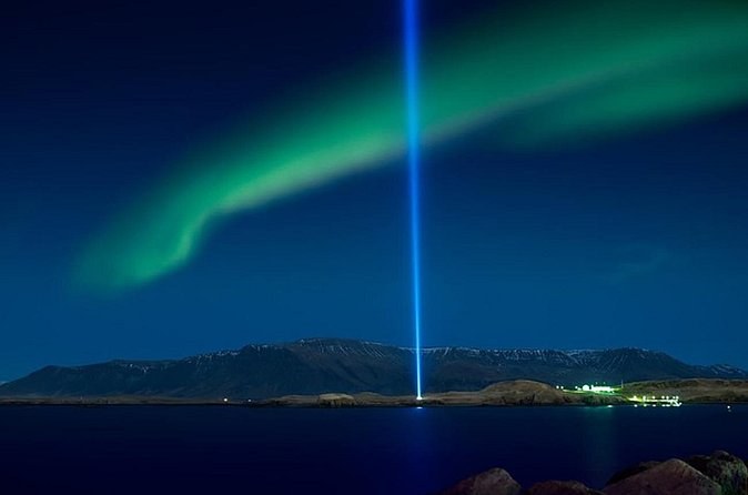 An aurora arc over a dark bay, a single beam of light rising from an island
