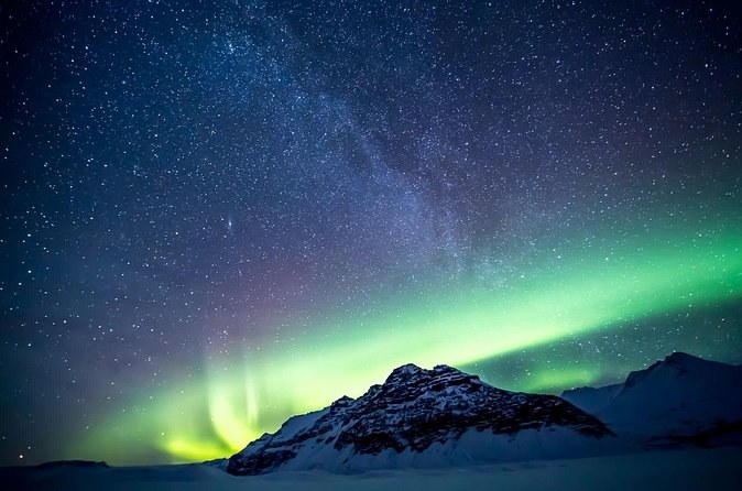 An aurora band and the Milky Way over a snow-covered peak