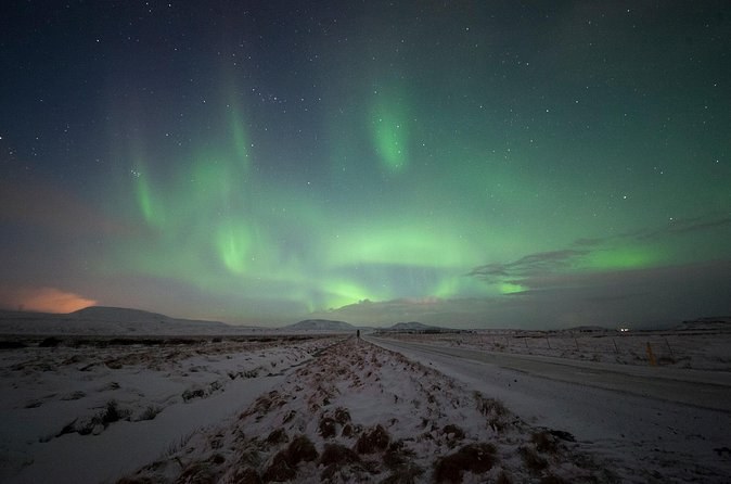 Faint green aurora over a snowy road running straight out into the dark