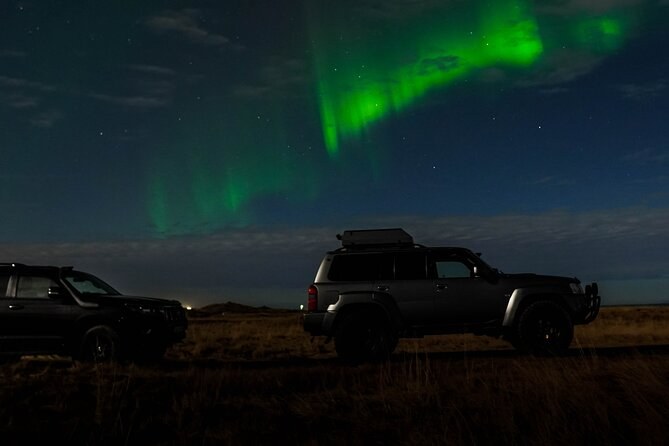 Two 4x4s parked on open ground under a band of green aurora
