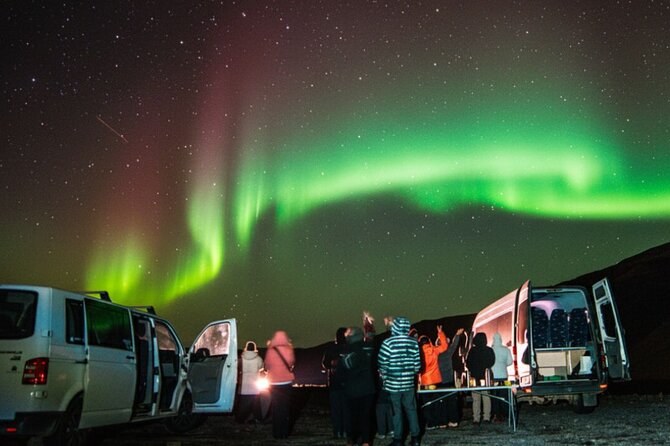 Minivans parked with their doors open while a group watches the aurora