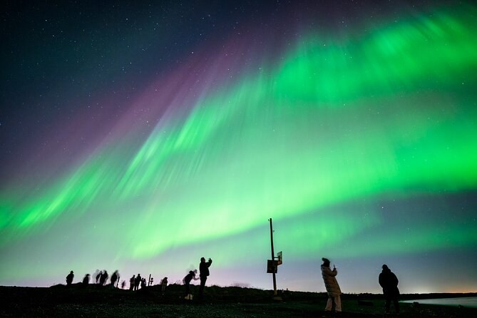 Silhouettes of watchers and tripods on a ridge under a wide aurora